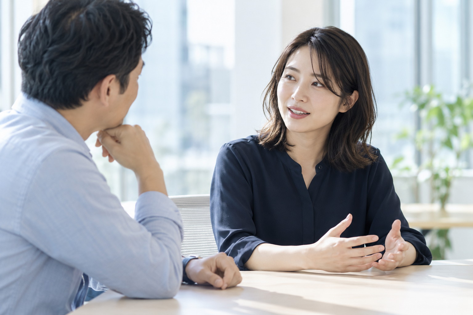明るいオフィスで、社員の話に同じ目線で耳を傾ける上司。生成したイメージ写真。